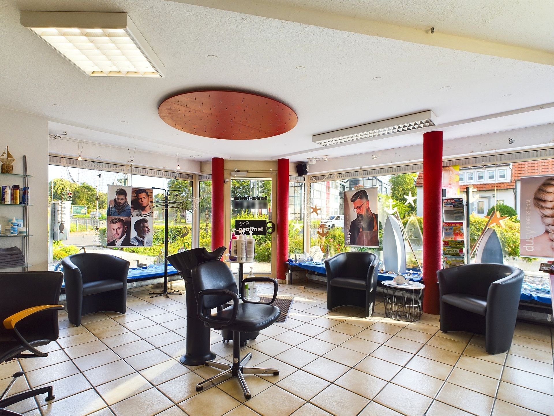 Moderner, heller Friseursalon mit mehreren Stühlen, Postern und großen Fenstern.