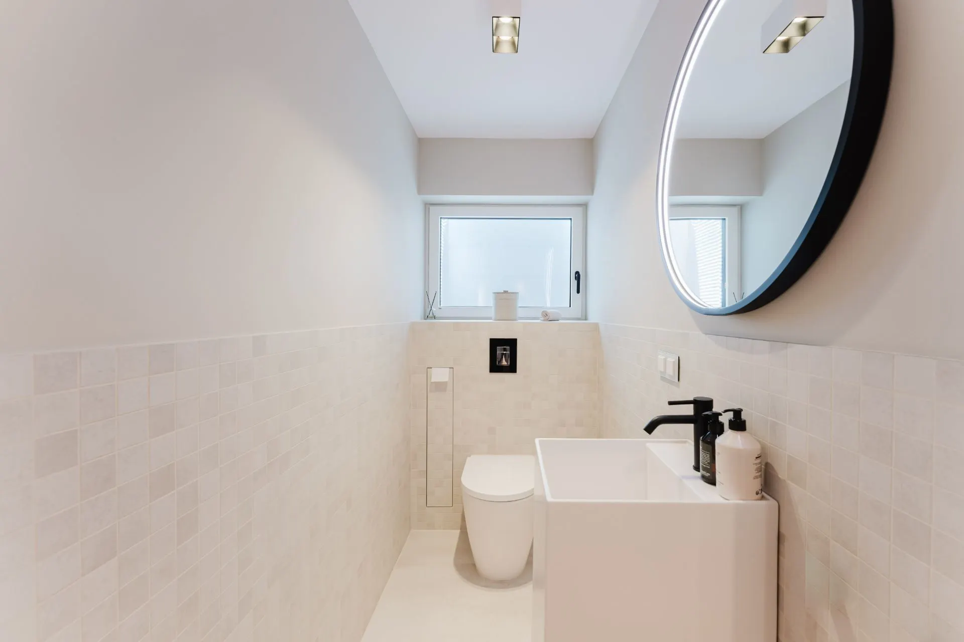 Modernes, schmales Badezimmer mit Toilette, Waschbecken und rundem Spiegel an der Wand.