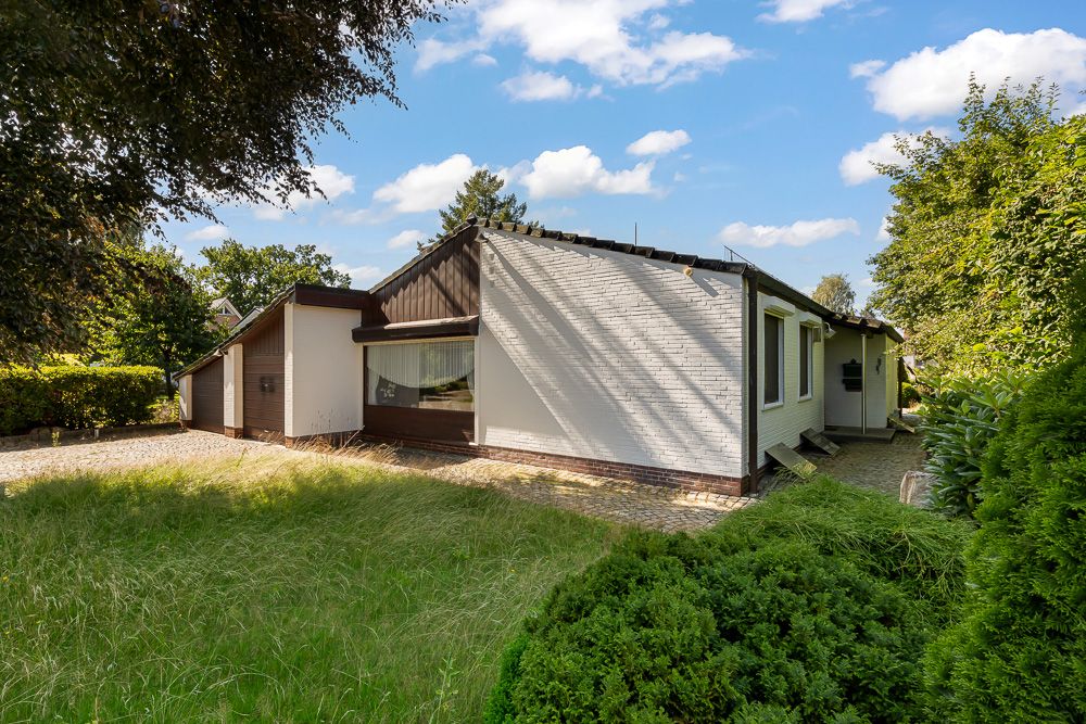 Einfamilienhaus mit weißer Fassade, großem Fenster und Garten im Vordergrund.