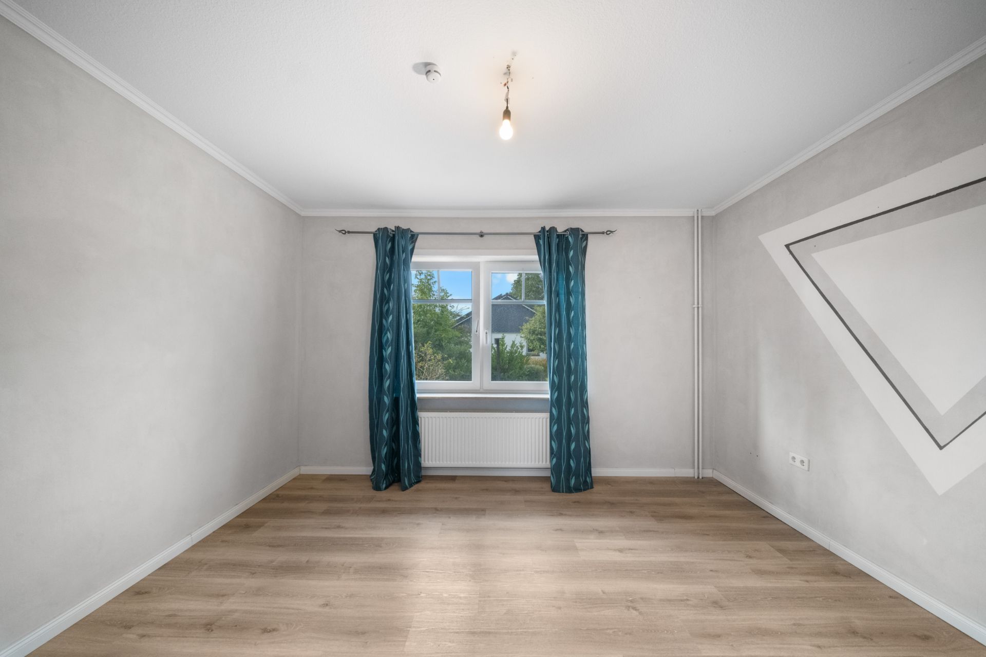 Leerer Raum mit Holzfußboden, Fenster mit blauen Vorhängen und weiß gestrichenen Wänden.