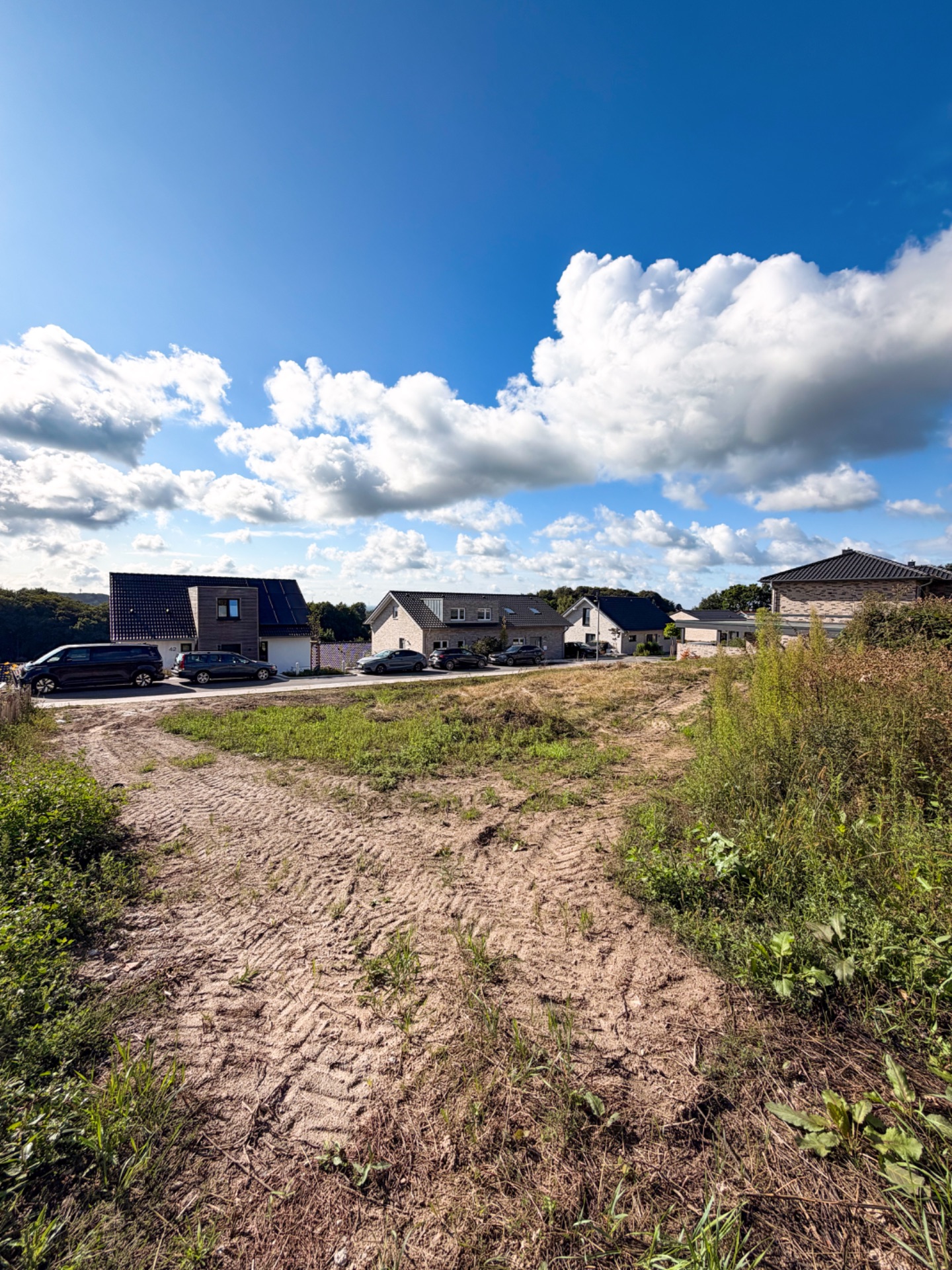 Blick auf eine Wohnstraße mit Einfamilienhäusern, Autos und blauem Himmel mit Wolken.