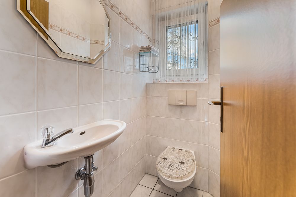 Kleines Badezimmer mit WC, Wandwaschbecken, Spiegel und Fenster mit Vorhang.