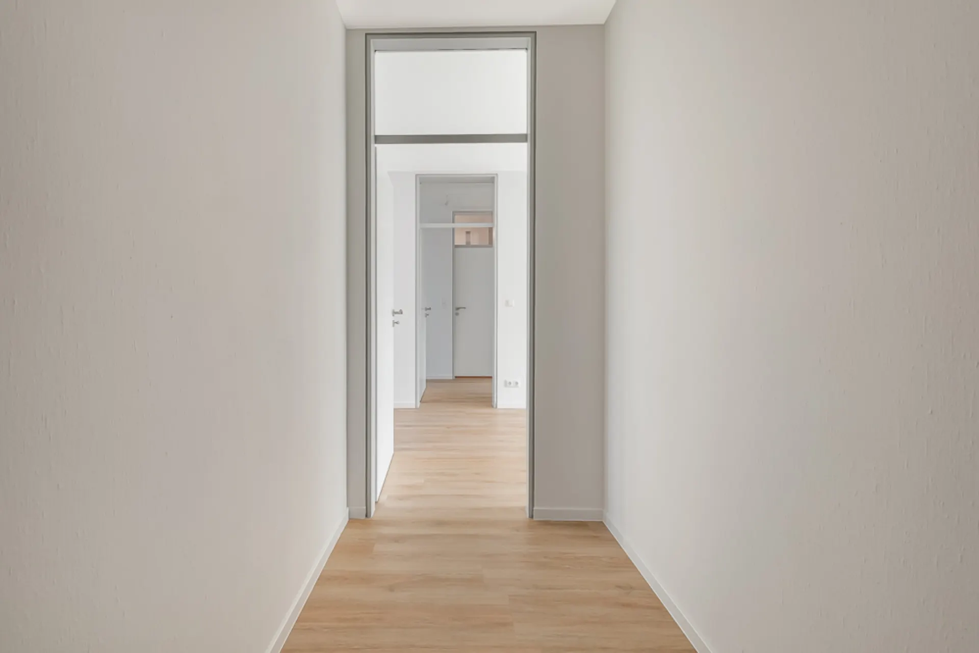 Heller Flur mit Holzboden und weißen Wänden, mehrere Türen am Ende sichtbar.