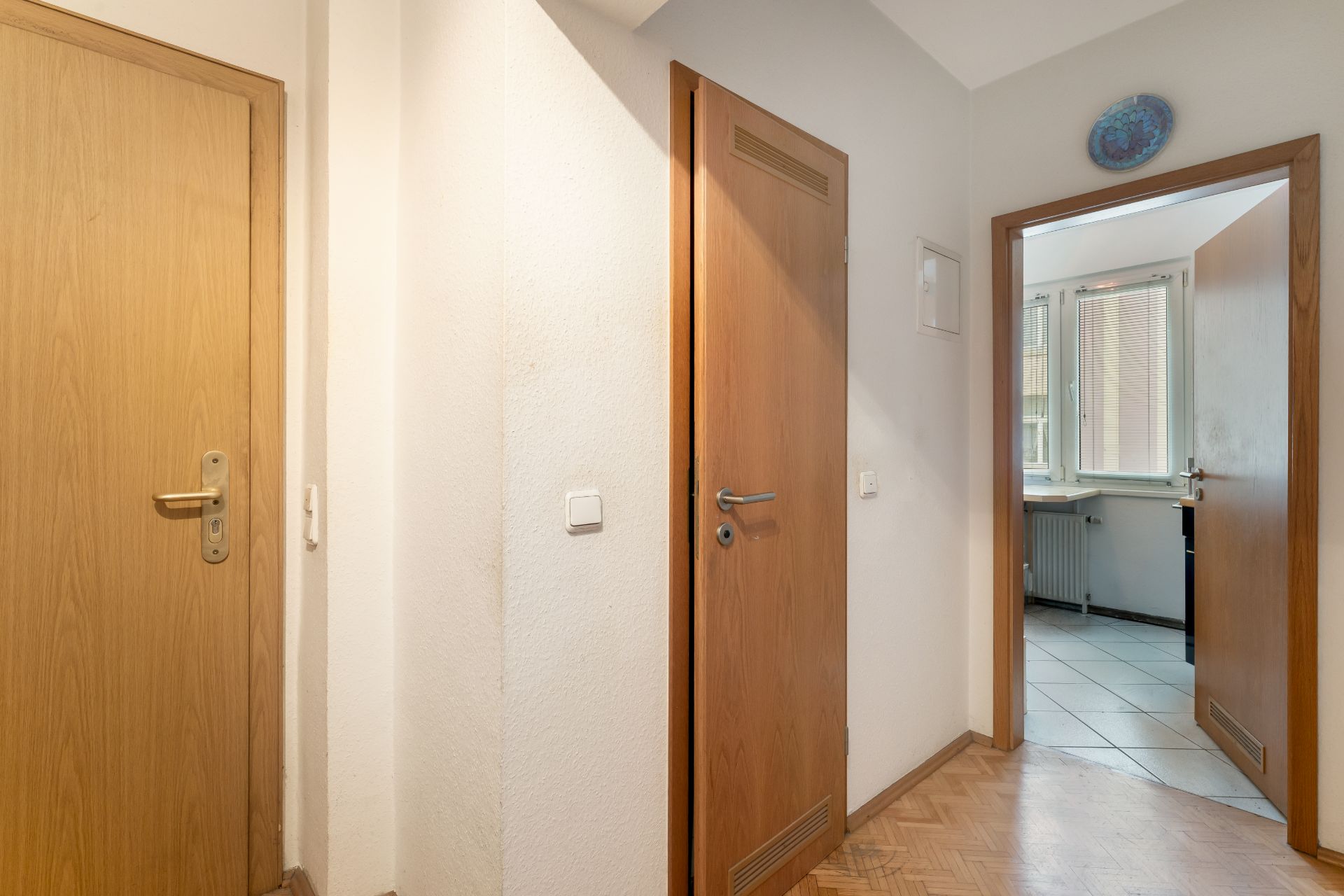 Flur mit drei Holztüren, eine offen mit Blick in einen hellen Raum mit Fenstern.