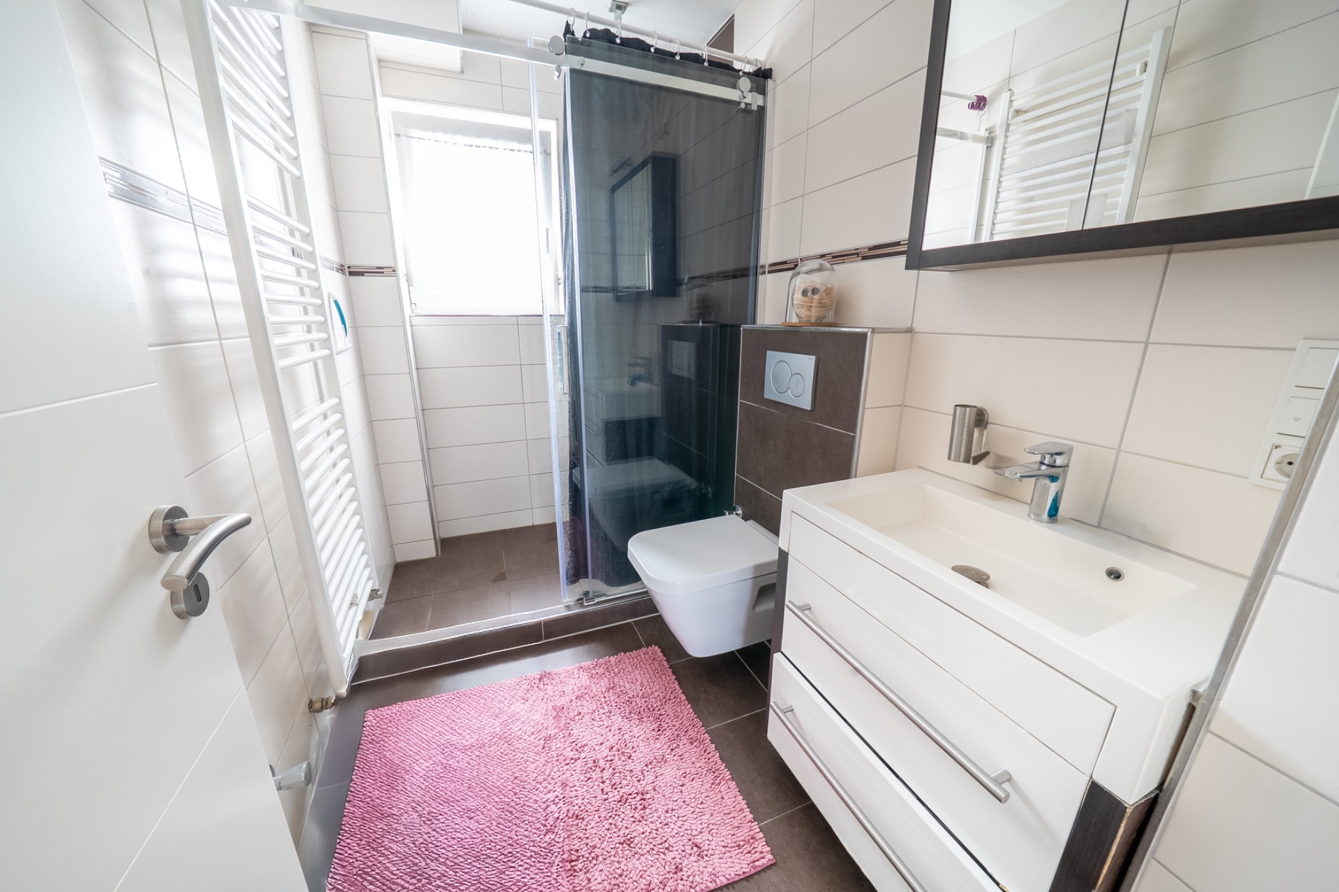 Modernes Badezimmer mit Dusche, Waschbecken, WC und rosa Teppich.
