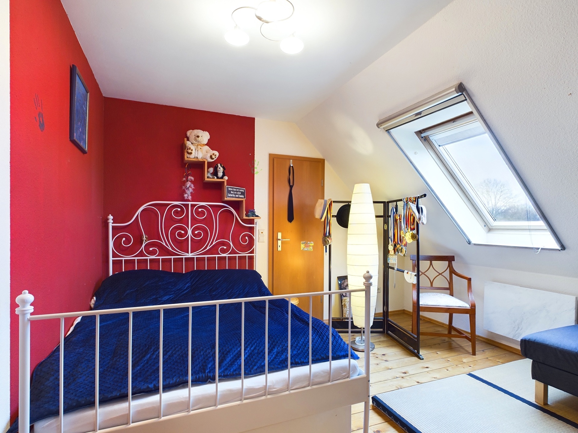 Helles Schlafzimmer mit Dachfenster, weißem Bettgestell und roter Wand.