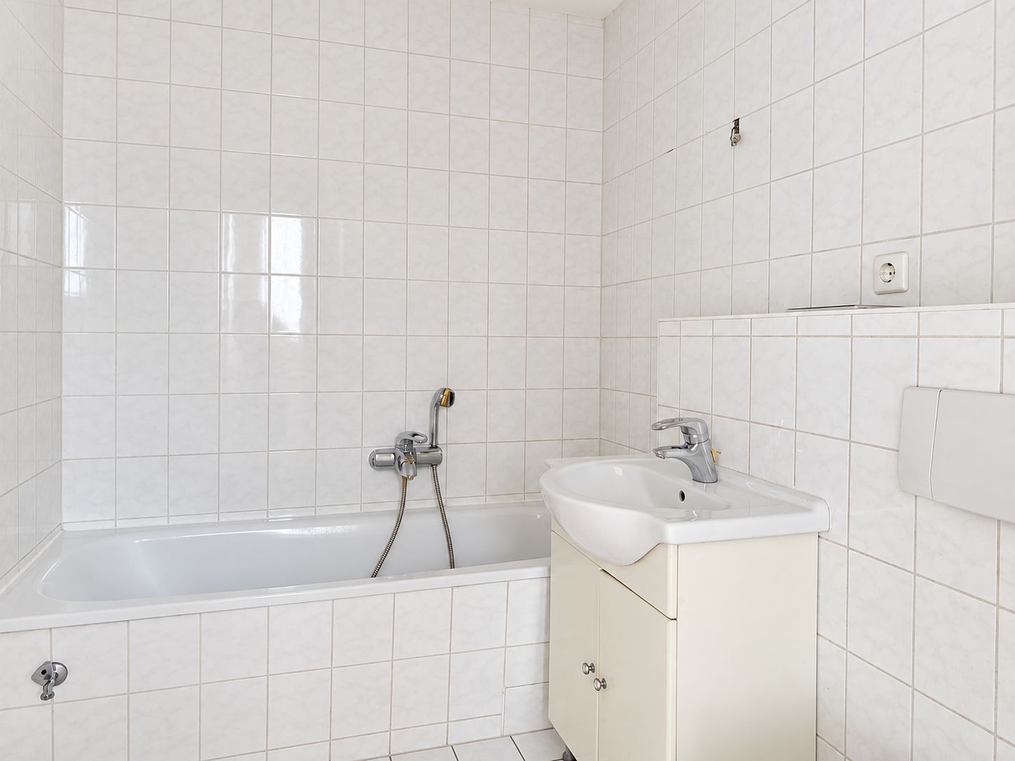 Helles Badezimmer mit Badewanne, Waschbecken und weißen Fliesen an Wand und Boden.