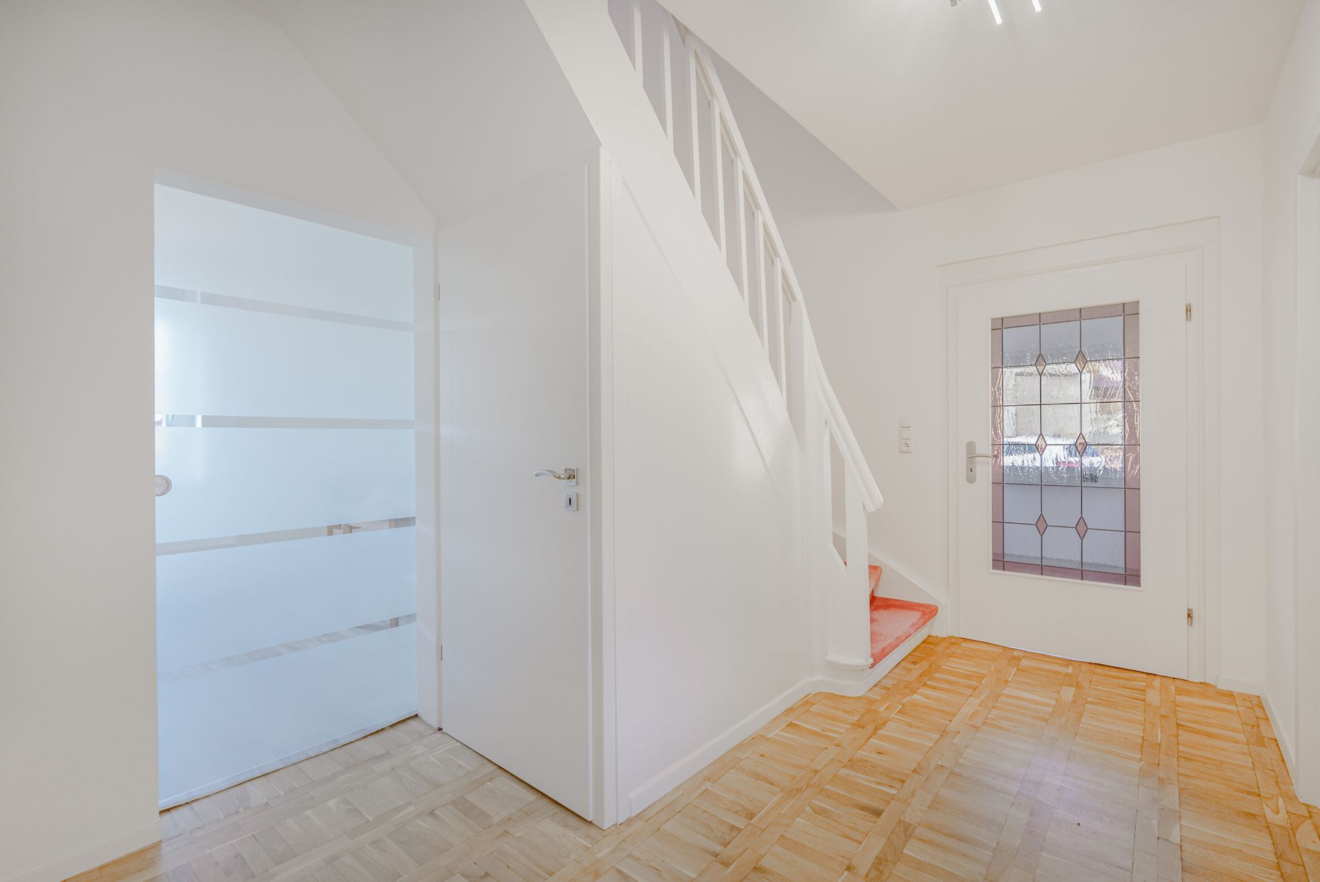 Heller Flur mit Holzfußboden, Treppe und Glastüren in einem Wohnhaus.