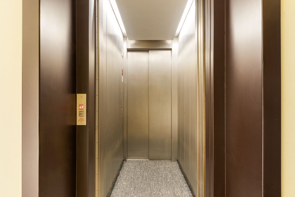 Geschlossener moderner Aufzug mit Edelstahlwänden und Teppichboden in einem Wohngebäude.
