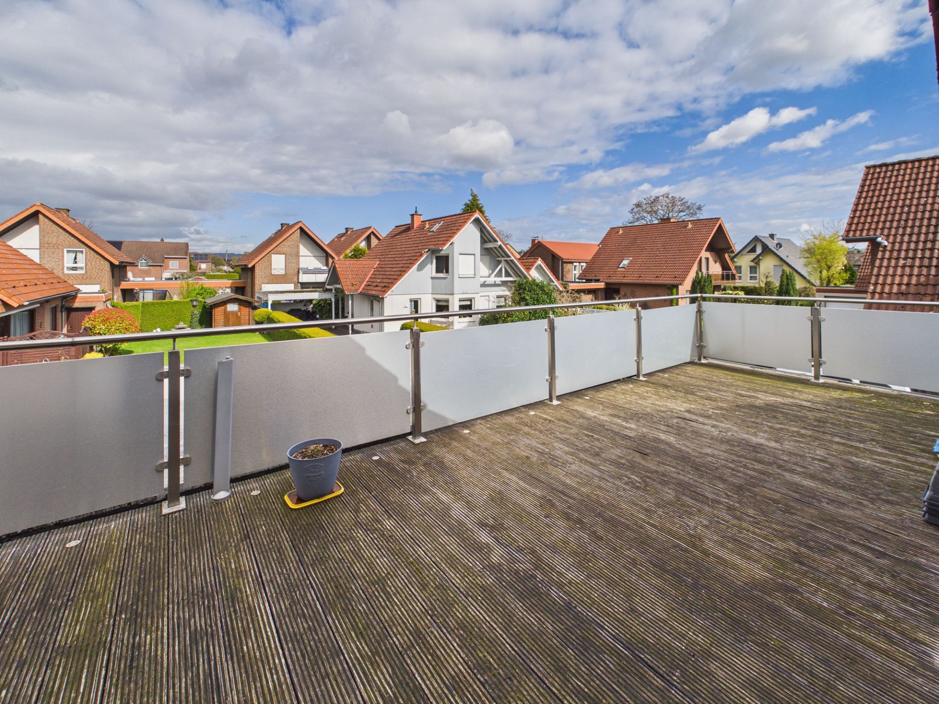 Große Terrasse mit Holzboden, Geländer und Blumentopf, umgeben von Wohnhäusern.