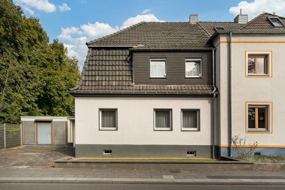 Wohnhaus mit grauem Dach, vier Fenstern und angrenzender Garage, davor Gehweg.
