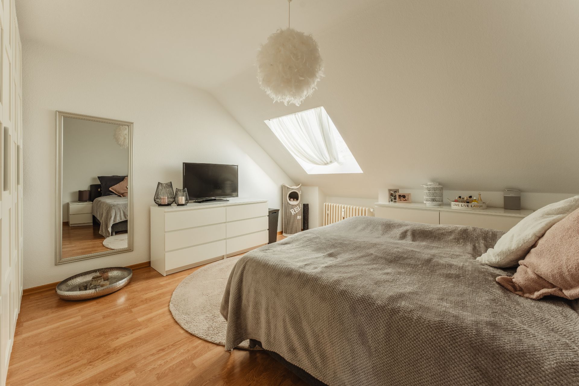 Helles Schlafzimmer mit Dachfenster, Bett, Kommode, Spiegel und Holzboden.