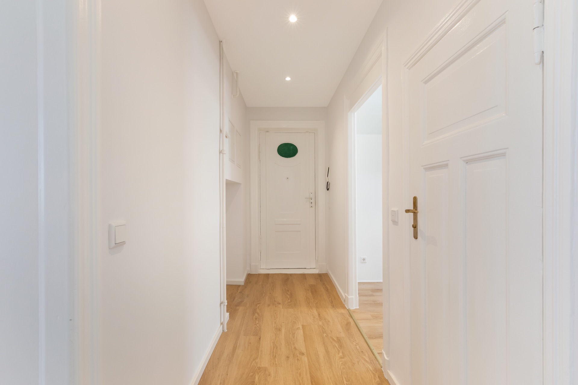 Heller Flur mit Holzboden, weißen Wänden und mehreren Türen in einer Wohnung.