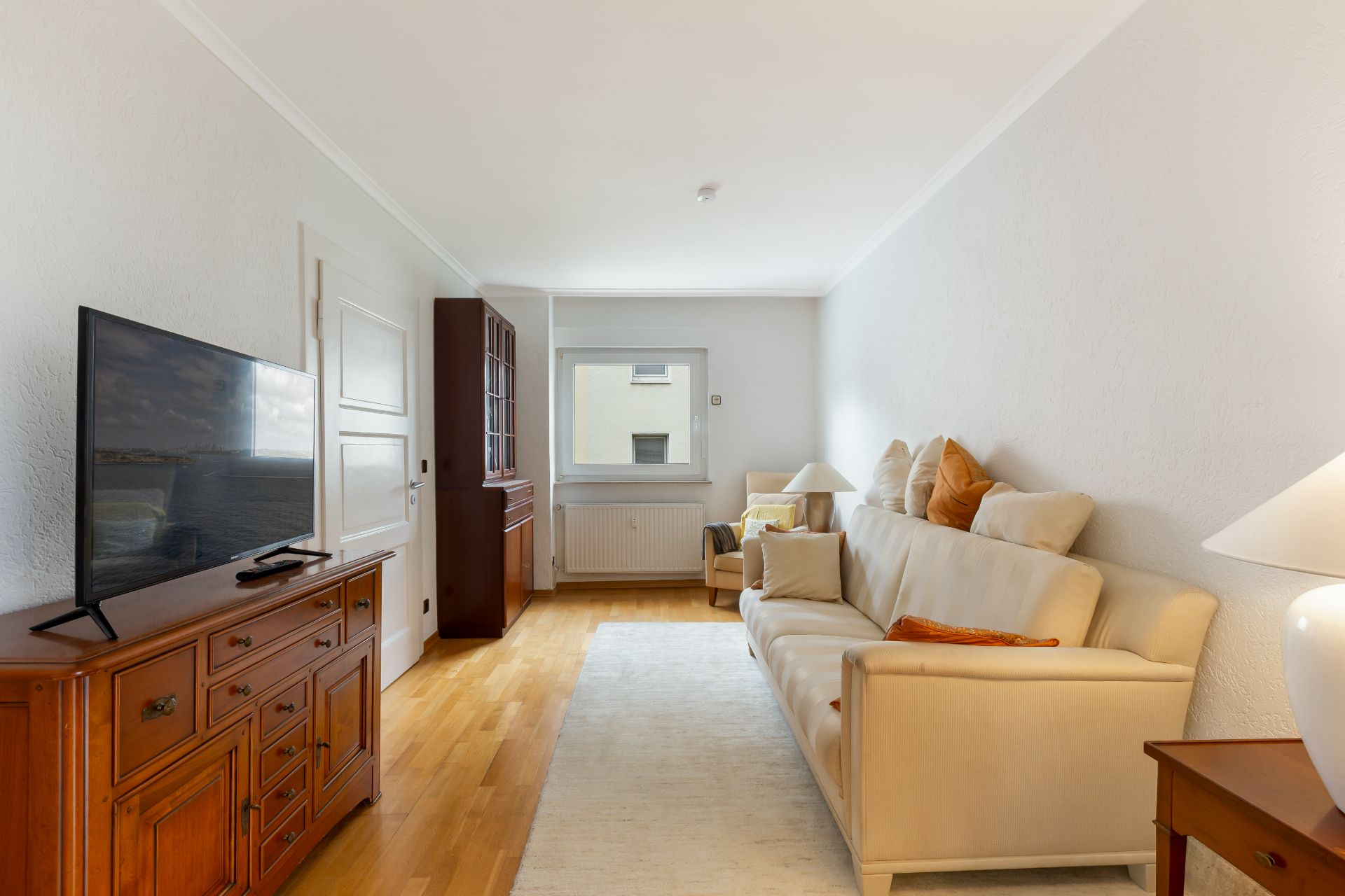 Wohnzimmer mit Sofa, Fernseher auf Holzkommode und Fenster im Hintergrund.