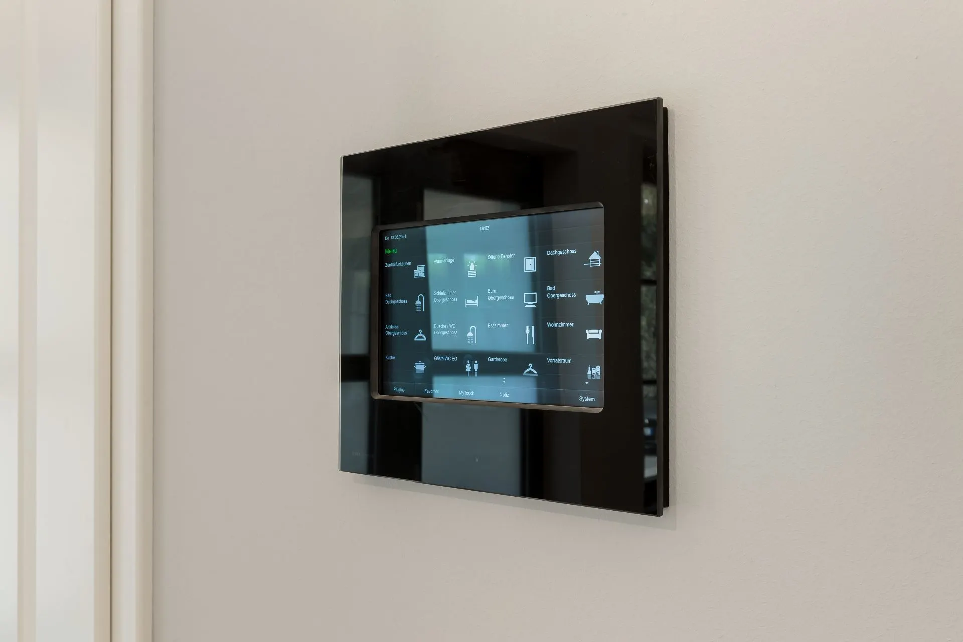 An einer weißen Wand ist ein modernes Touchpanel-Steuergerät montiert.