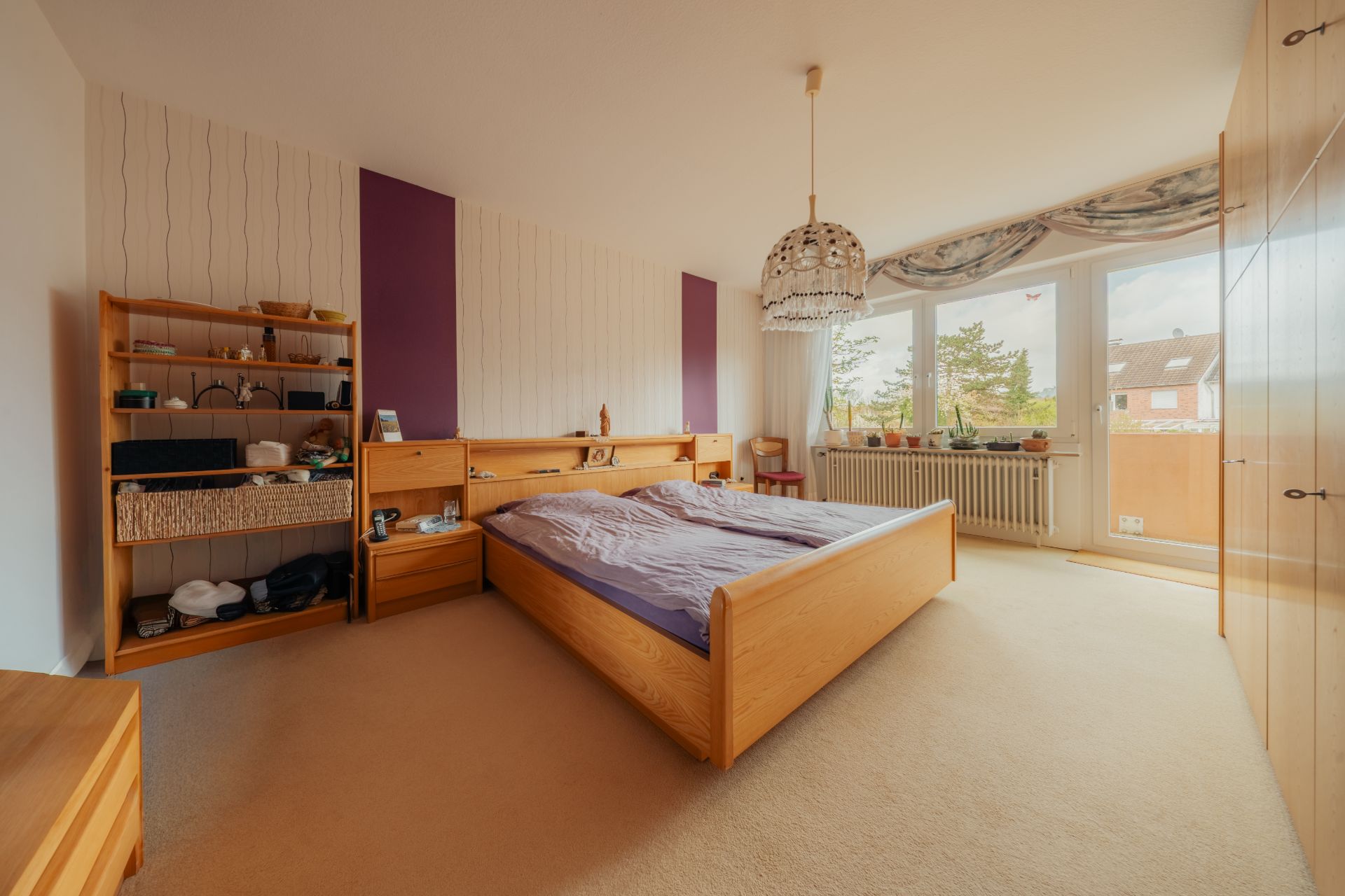 Helles Schlafzimmer mit großem Holzbett, Regal, Kleiderschrank und Fenster mit Blick nach draußen.