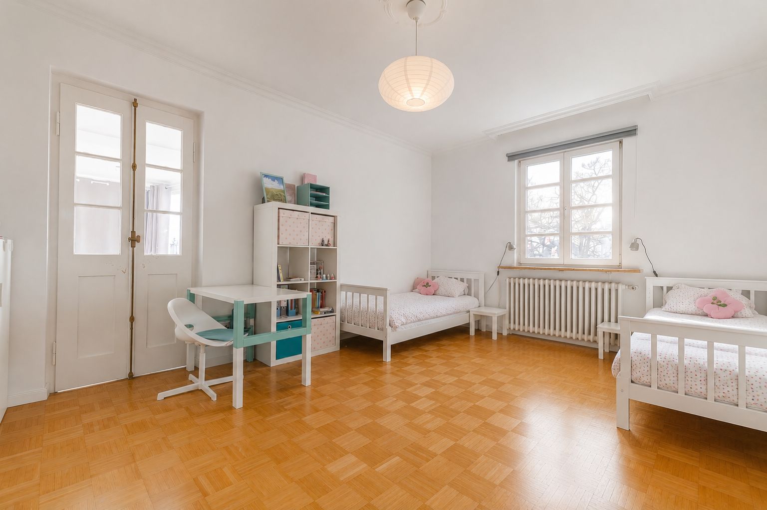 Helles Kinderzimmer mit zwei Einzelbetten, Schreibtisch, Stuhl und Regal auf Parkettboden.