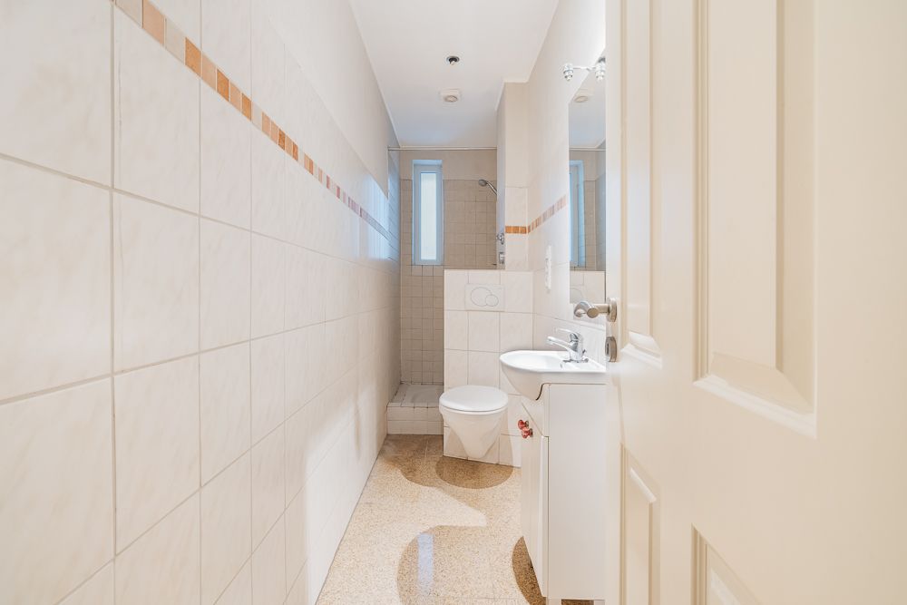 Helles Badezimmer mit Dusche, Toilette und Waschbecken, Wände und Boden sind gefliest.