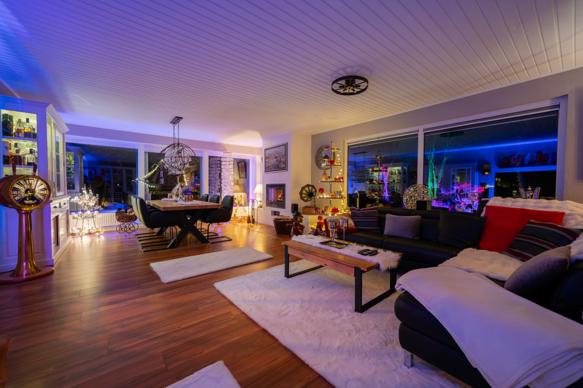Modernes Wohnzimmer mit Sofa, Esstisch, Beleuchtung und großen Fenstern, Holzboden und Teppichen.