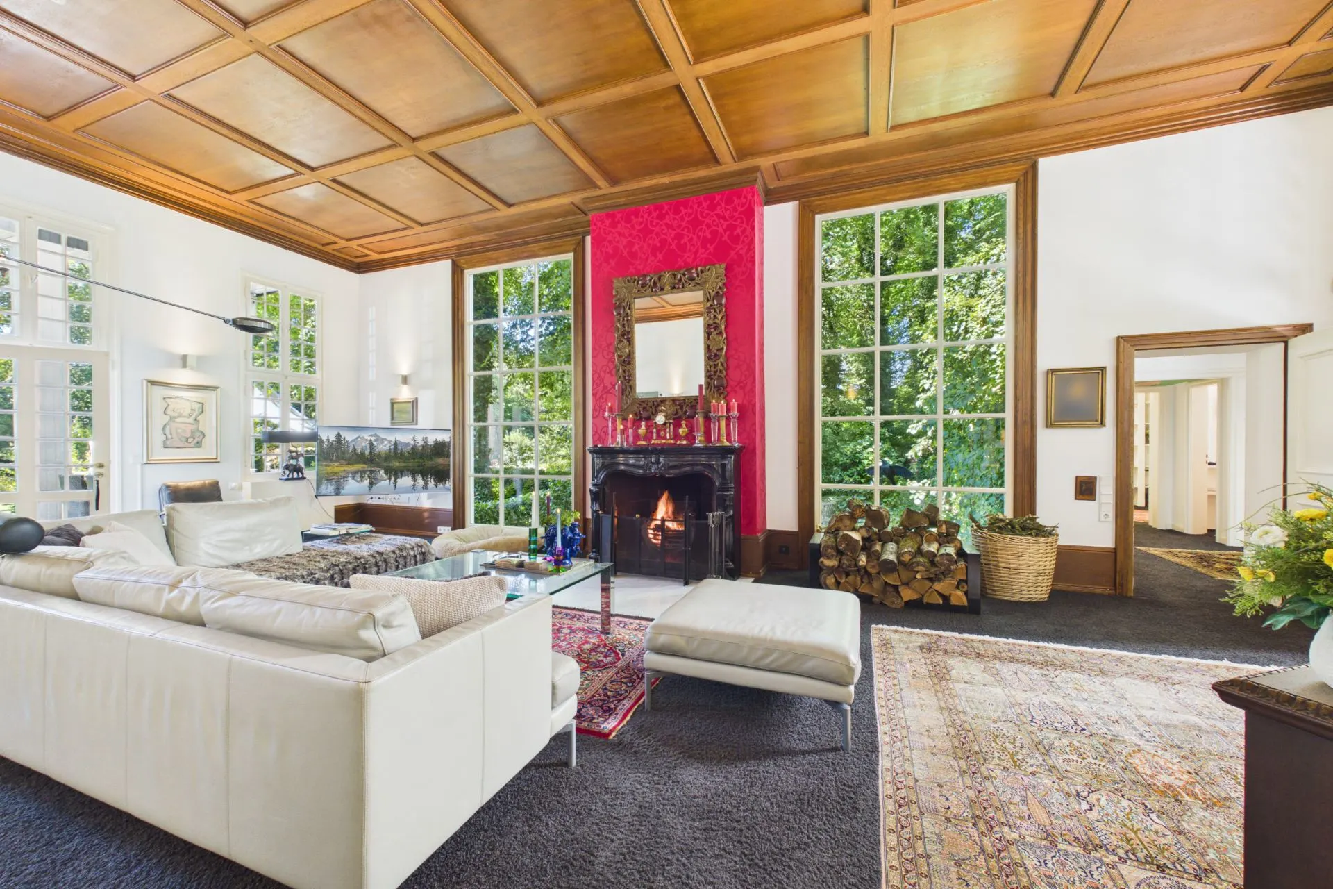 Großes Wohnzimmer mit Kamin, weißen Sofas, großen Fenstern und Holzdecke.
