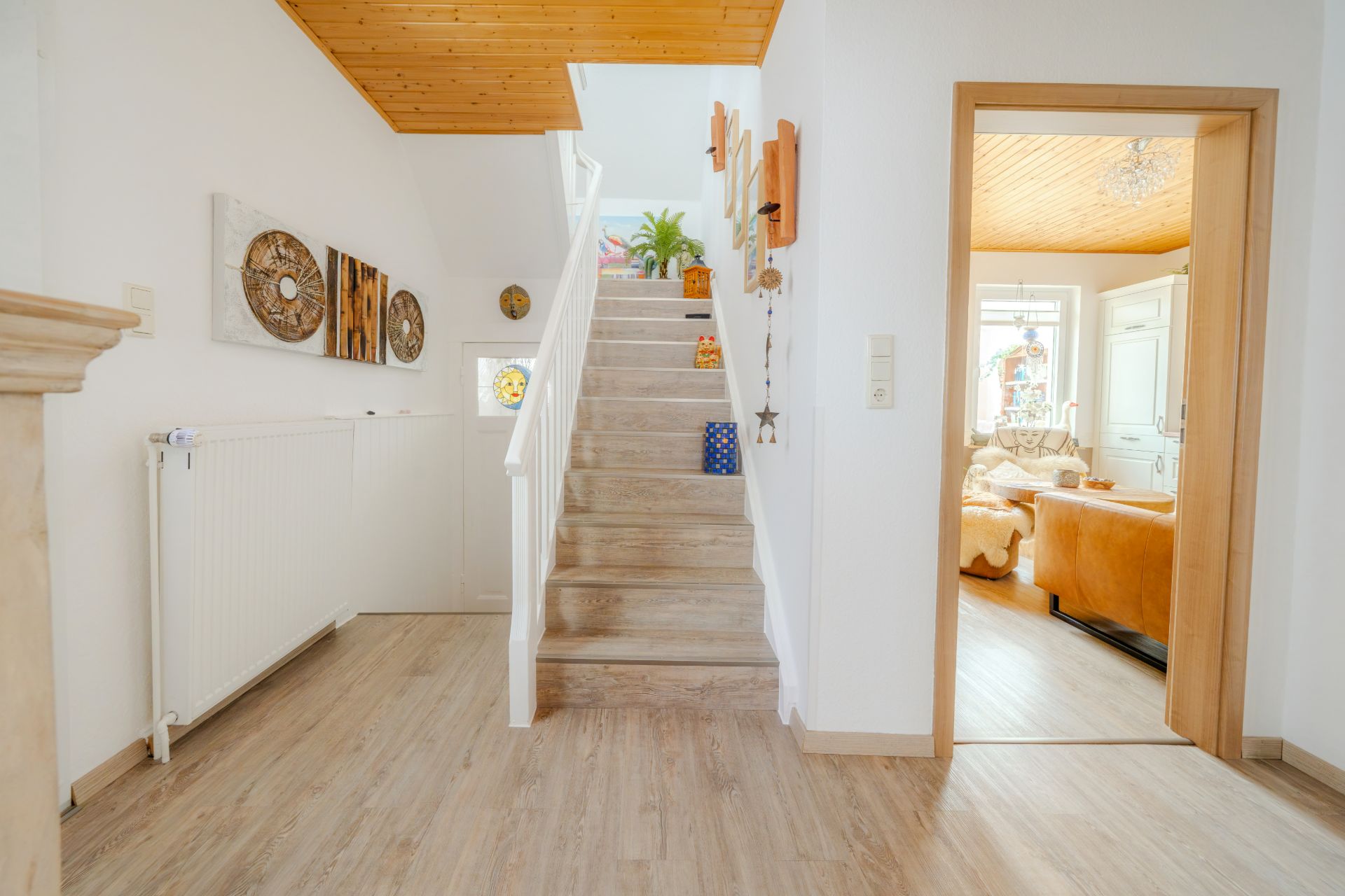 Heller Flur mit Holztreppe, Dekoration an der Wand und Blick ins Wohnzimmer.