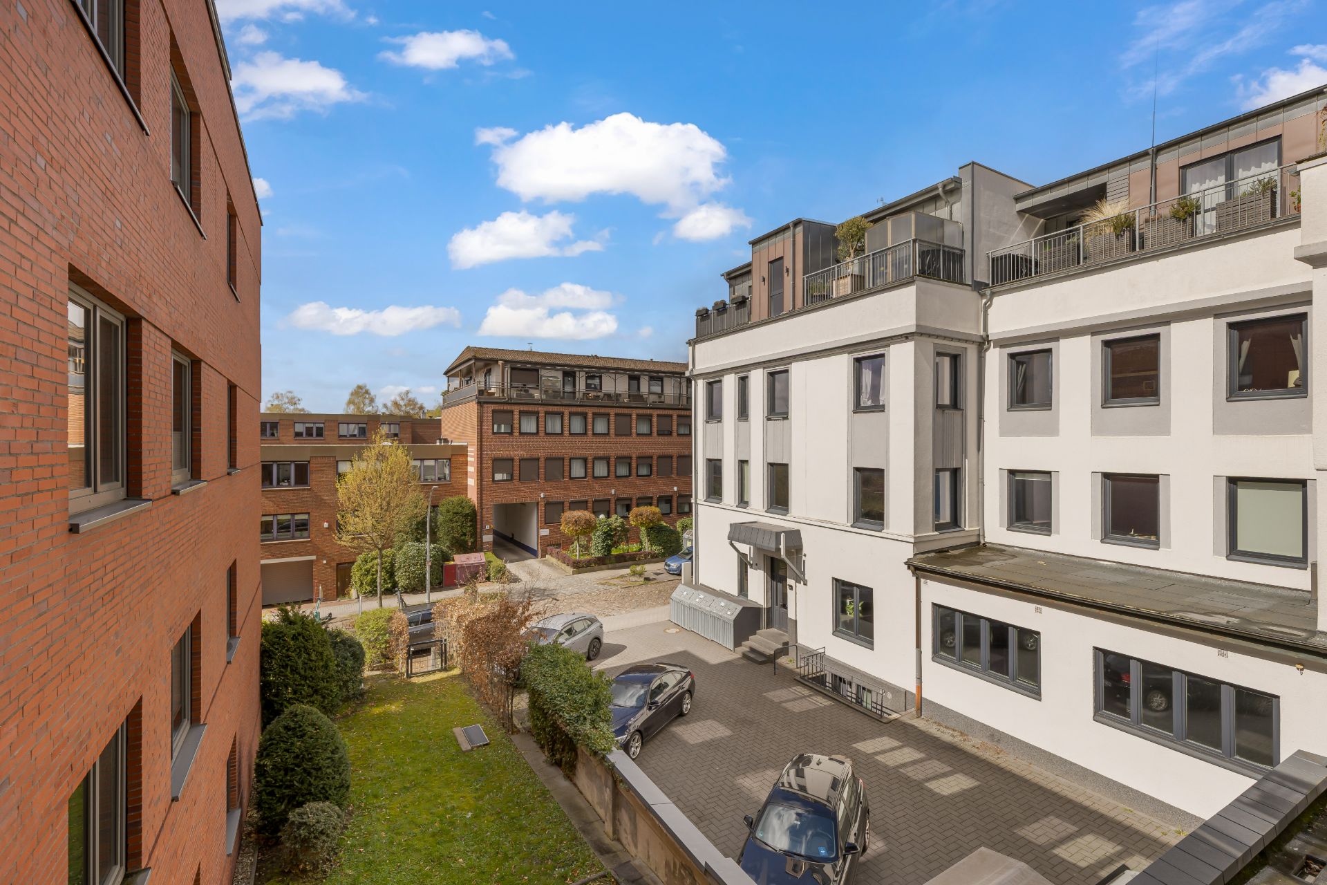 Mehrere Wohngebäude mit Innenhof, Autos und kleinen Grünflächen bei Tageslicht.