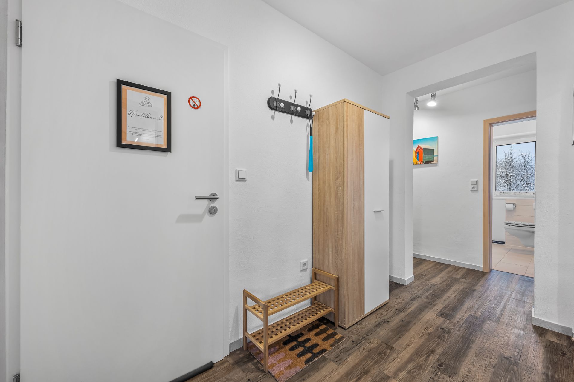 Heller Flur mit Holzschuhregal, Garderobe, Schrank und Blick ins Badezimmer.