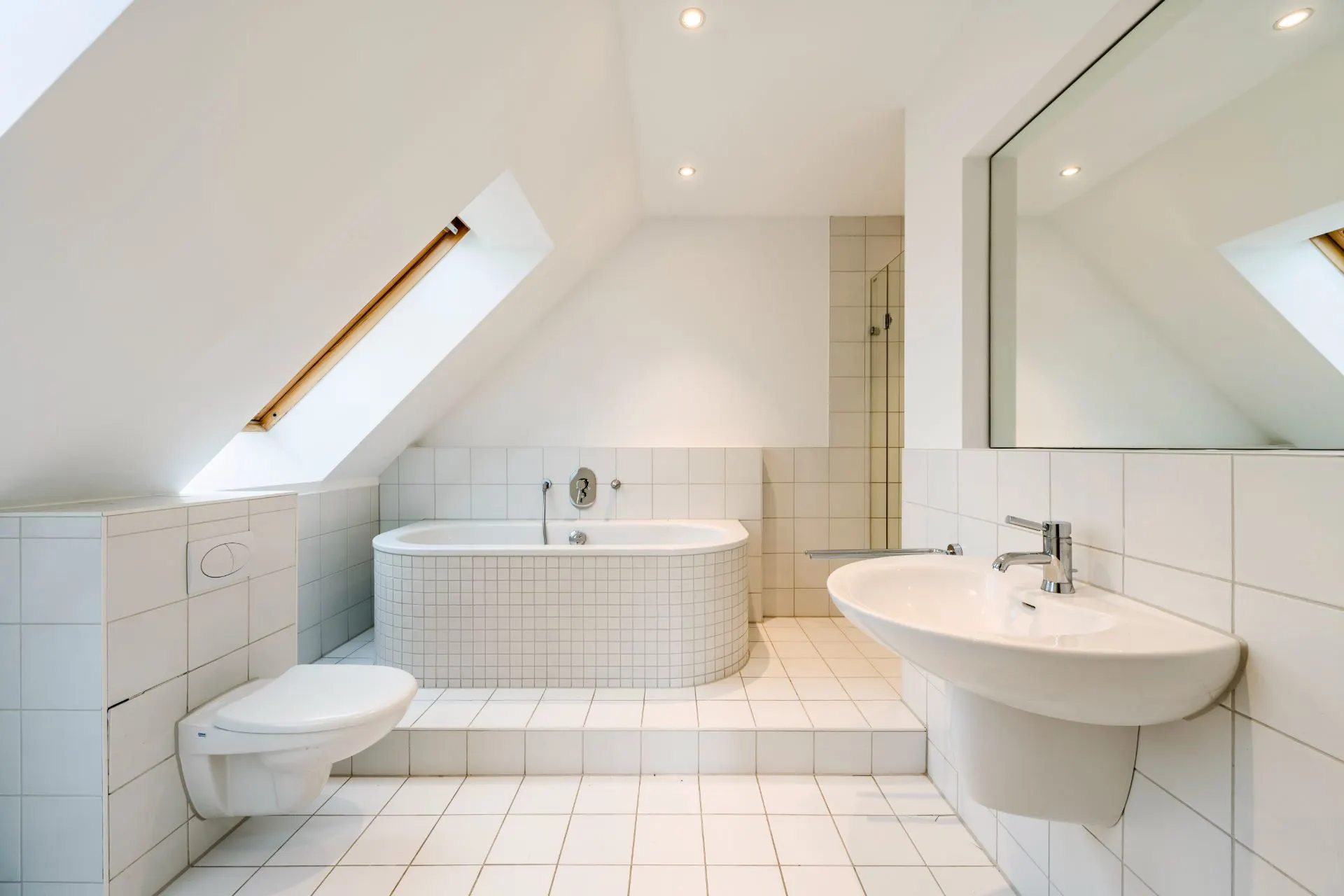 Modernes Badezimmer mit Badewanne, Wandtoilette, Waschtisch und großem Spiegel unter Dachschräge.