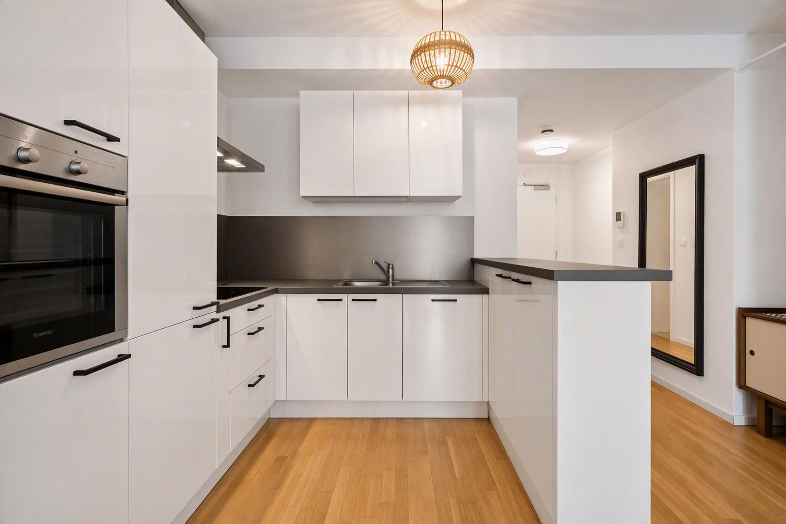 Moderne weiße Einbauküche mit Holzfußboden und Hängelampe.