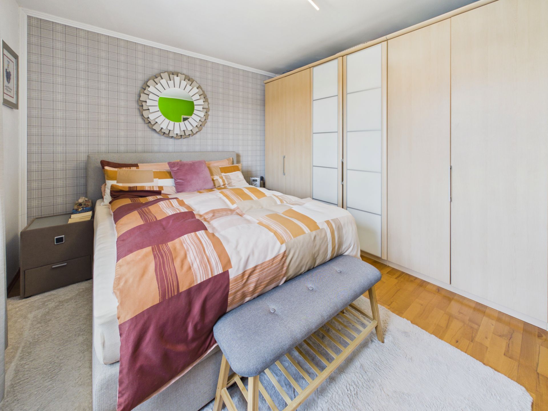 Schlafzimmer mit Doppelbett, großem Kleiderschrank und Sitzbank auf Holzfußboden.