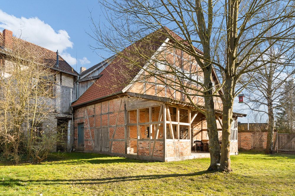 Backsteinhaus mit Holzbalken und großem Baum im Garten bei sonnigem Wetter.