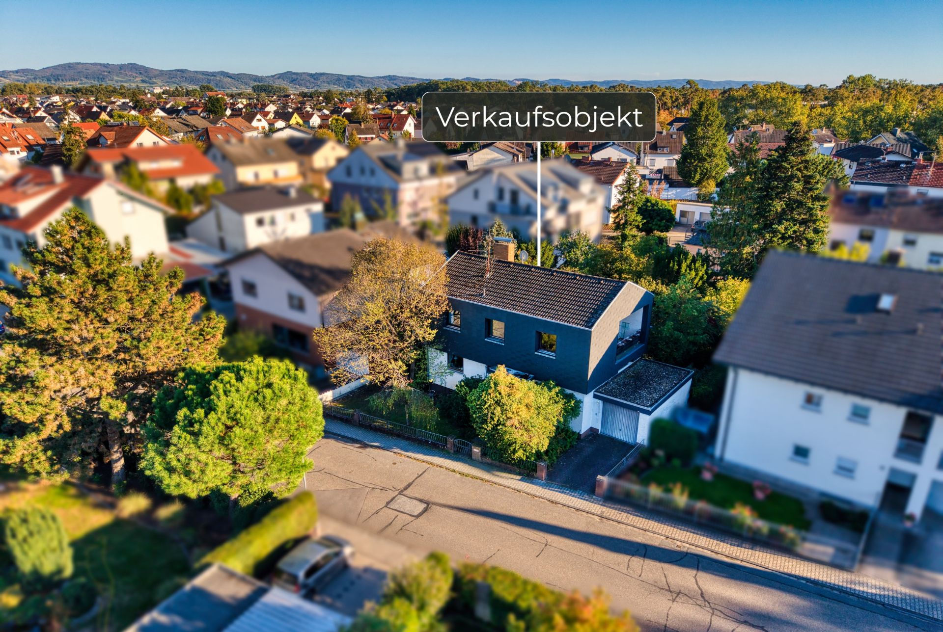 Luftaufnahme eines Einfamilienhauses mit Garten in einer Wohngegend, Schild mit 'Verkaufsobjekt' darüber.