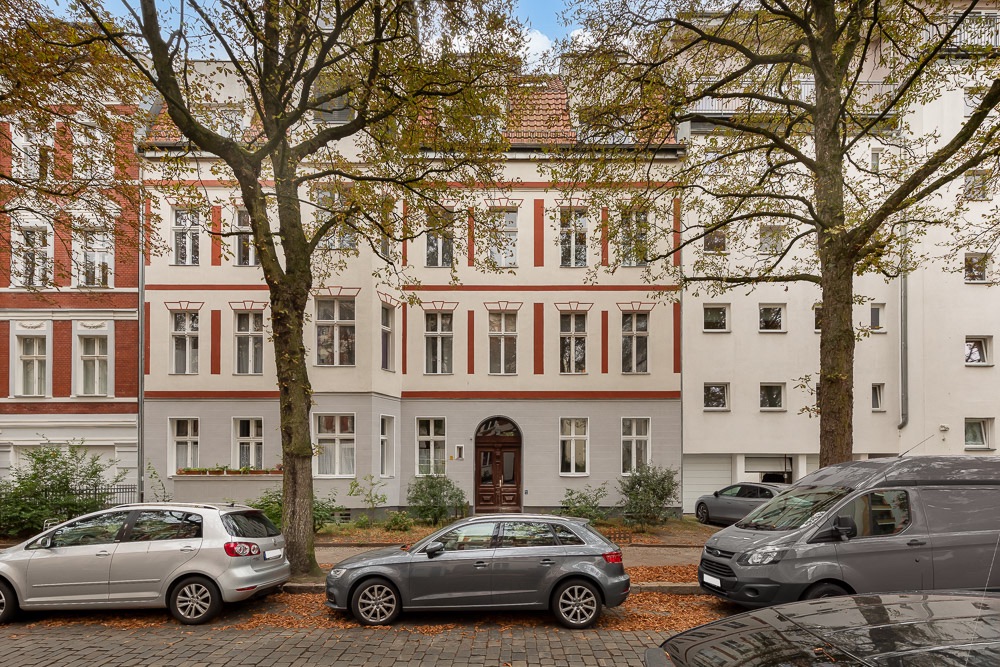 Mehrstöckiges Wohnhaus mit Bäumen davor und Autos am Straßenrand geparkt.