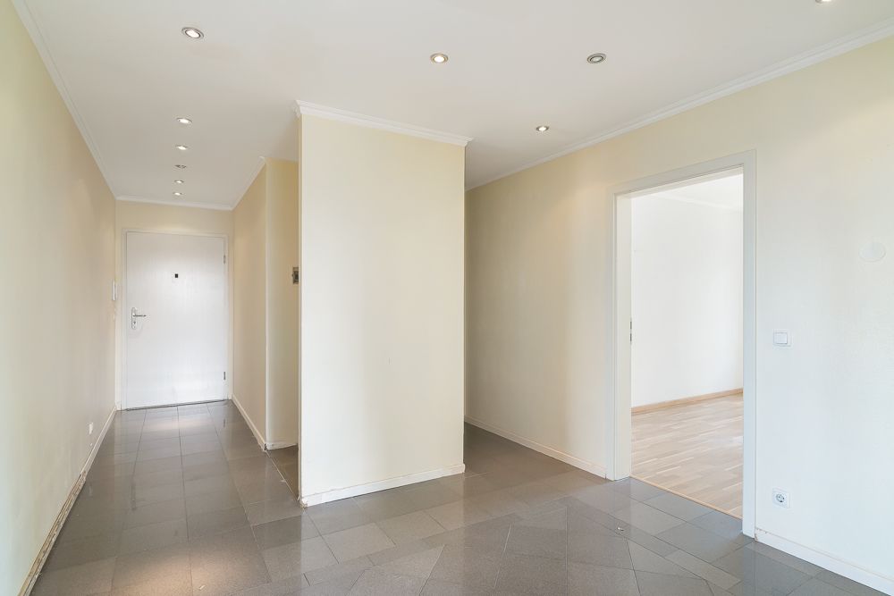 Heller Flur mit Fliesenboden und Zugang zu einem weiteren Raum, weiße Wände und Decke.