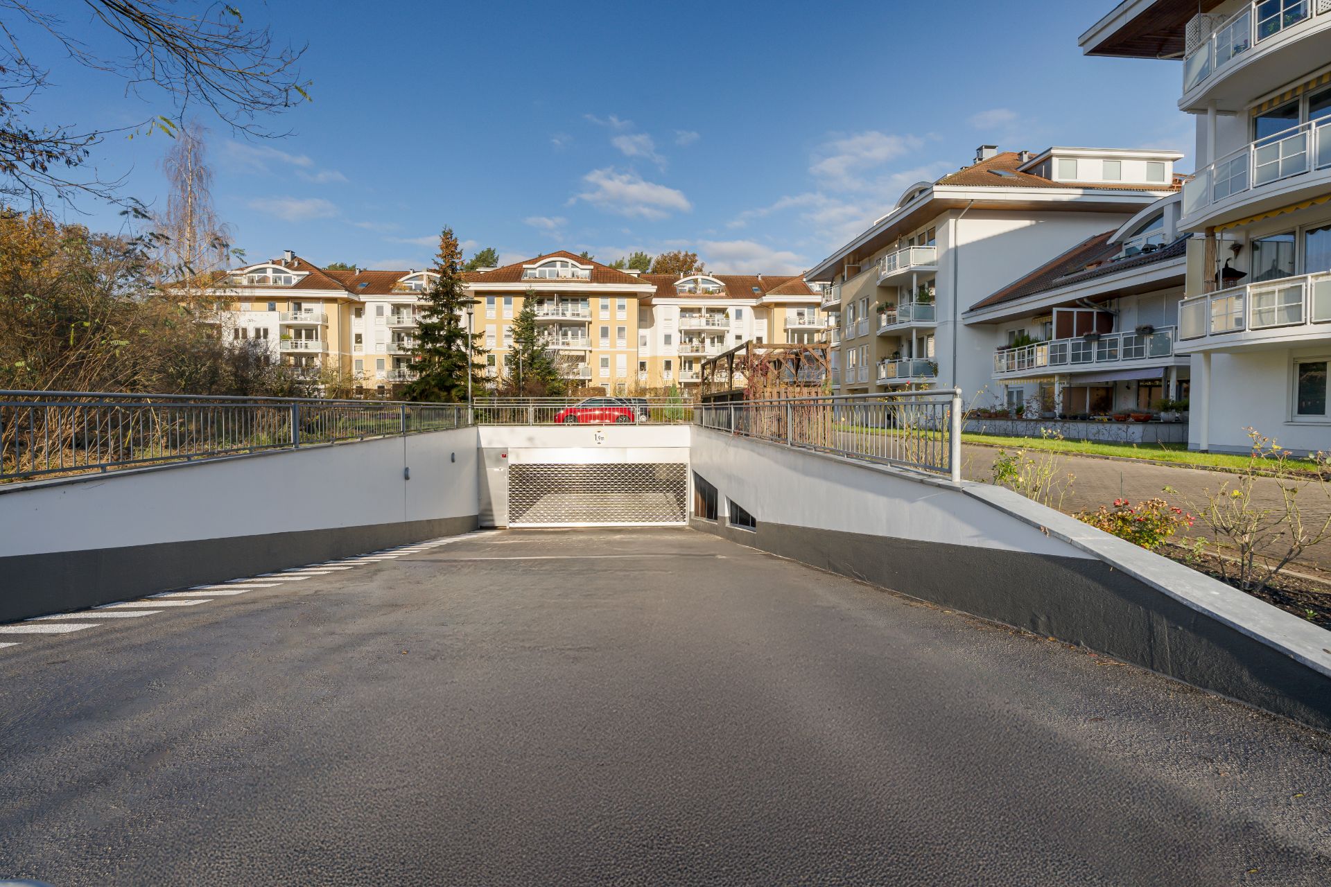 Einfahrt zu einer Tiefgarage vor mehreren Wohngebäuden bei sonnigem Wetter.