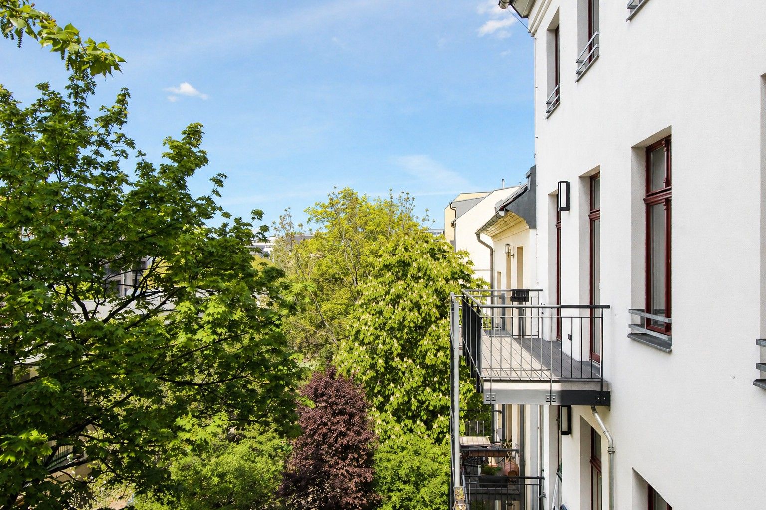 Balkone eines Wohnhauses mit Blick auf grüne Bäume und blauen Himmel.