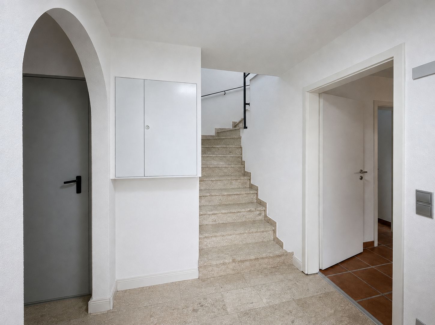 Heller Flur mit Steintreppe, weißen Wänden und mehreren Türen.