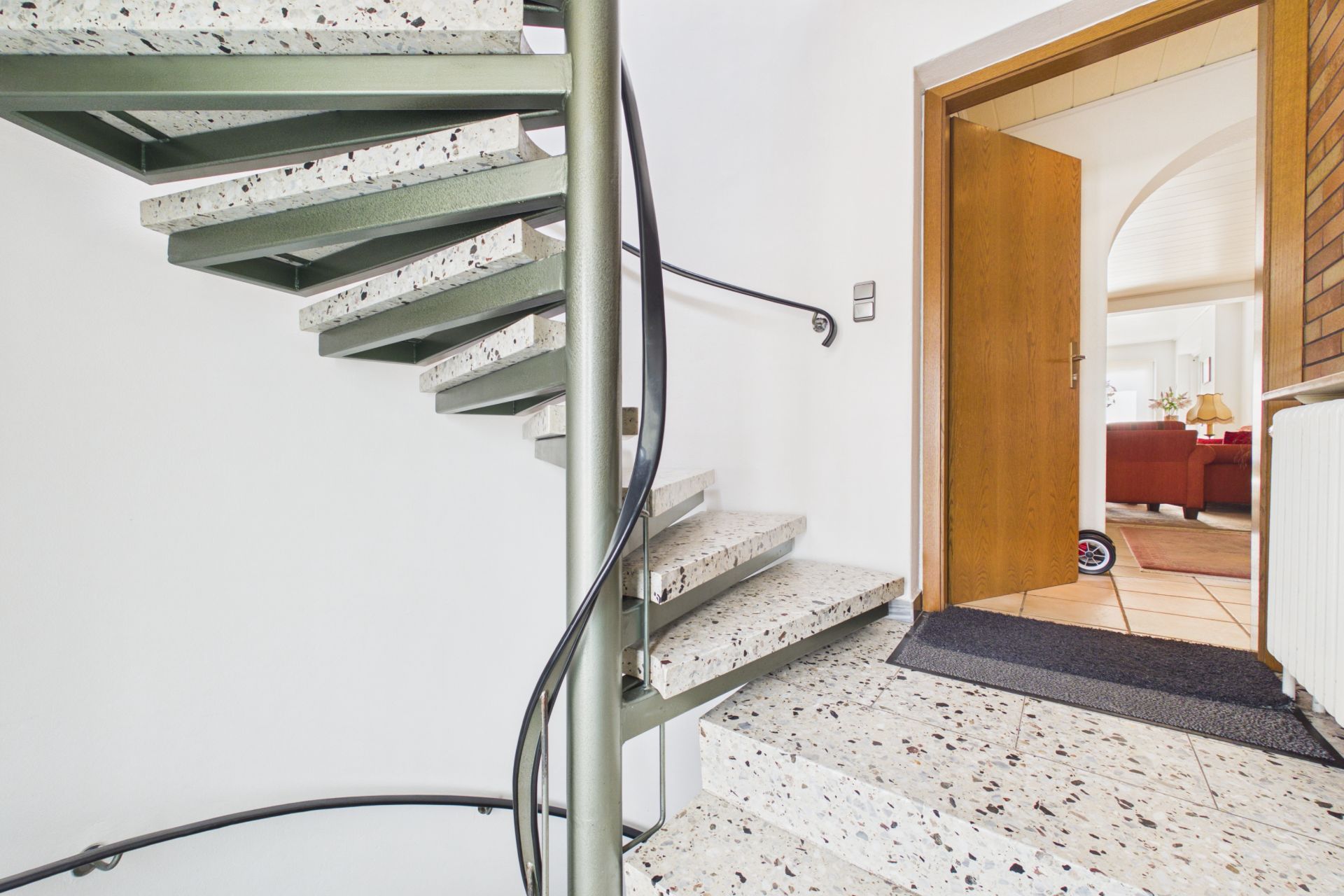 Eine Wendeltreppe aus Terrazzo neben einer geöffneten Holztür in einem Flur.