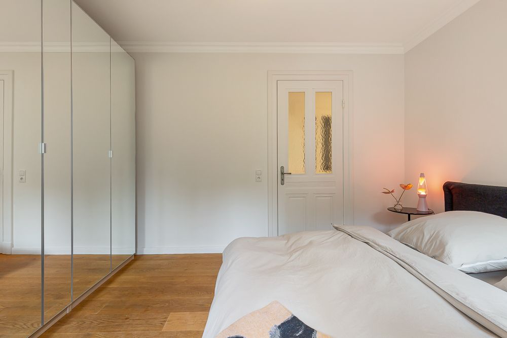 Schlafzimmer mit großem Spiegelkleiderschrank, Bett und Nachttisch mit Lampe.