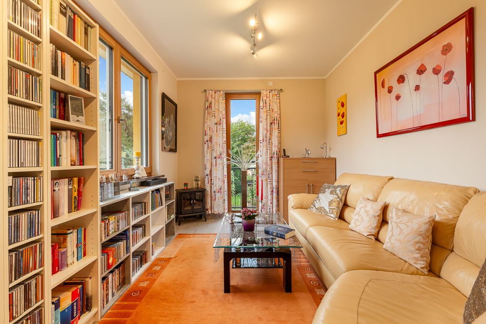 Helles Wohnzimmer mit Bücherregal, Ledersofa, Glastisch und großem Fenster mit Blick ins Grüne.