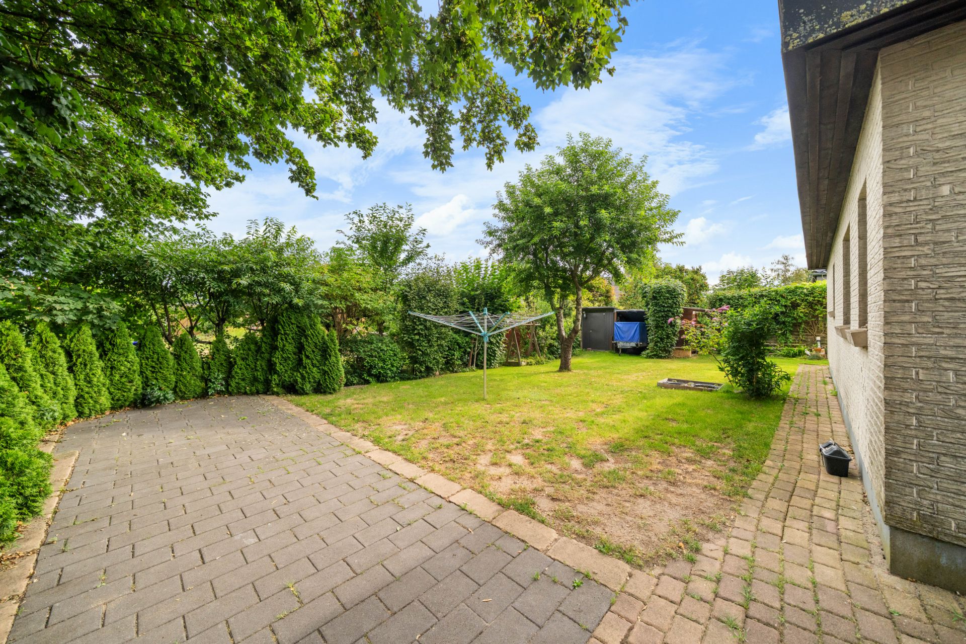 Gepflasterter Weg neben einem Garten mit Baum, Wäschespinne und Gartenhaus.