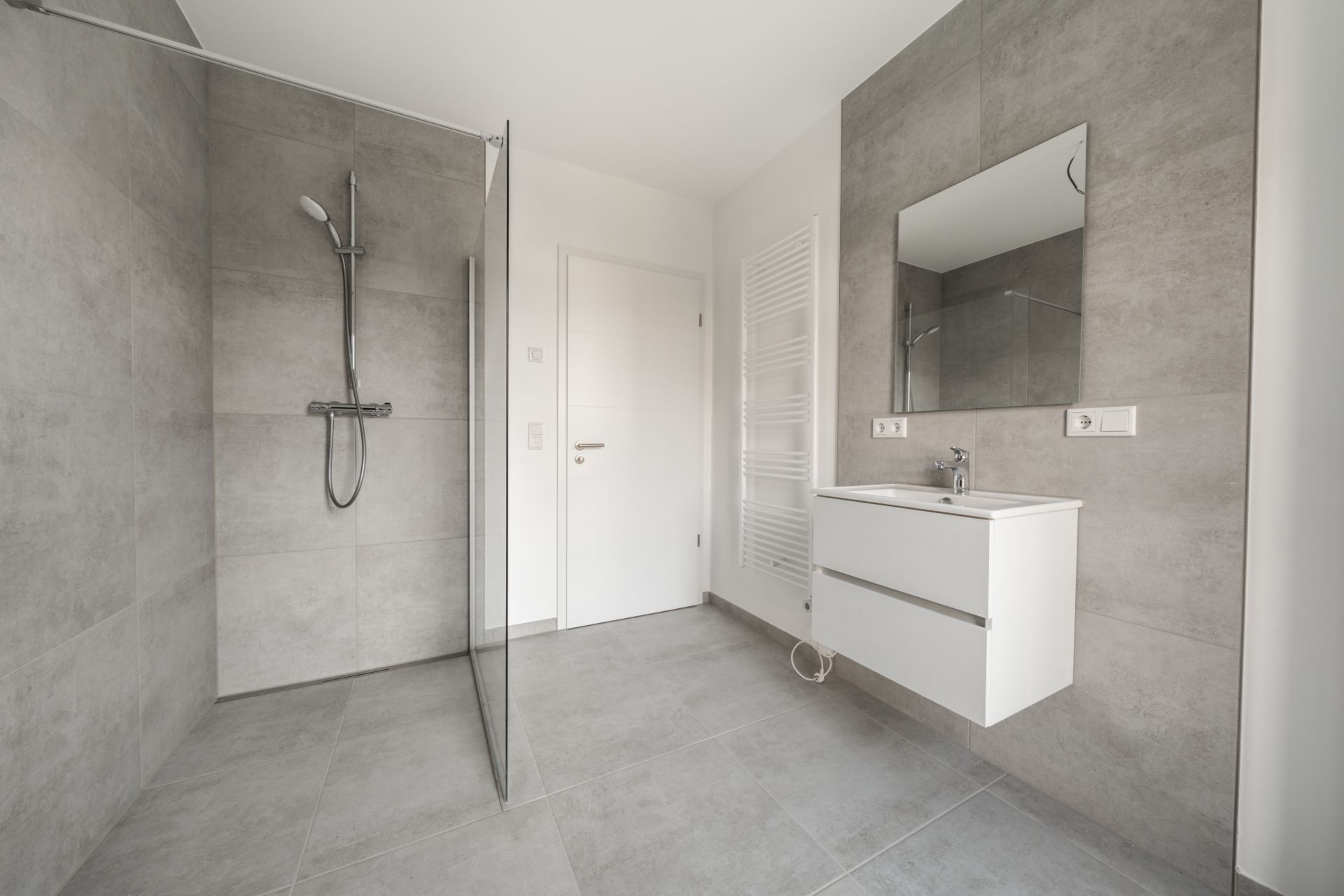 Modernes Bad mit bodengleicher Dusche, Waschbecken, Spiegel und hellen Fliesen.