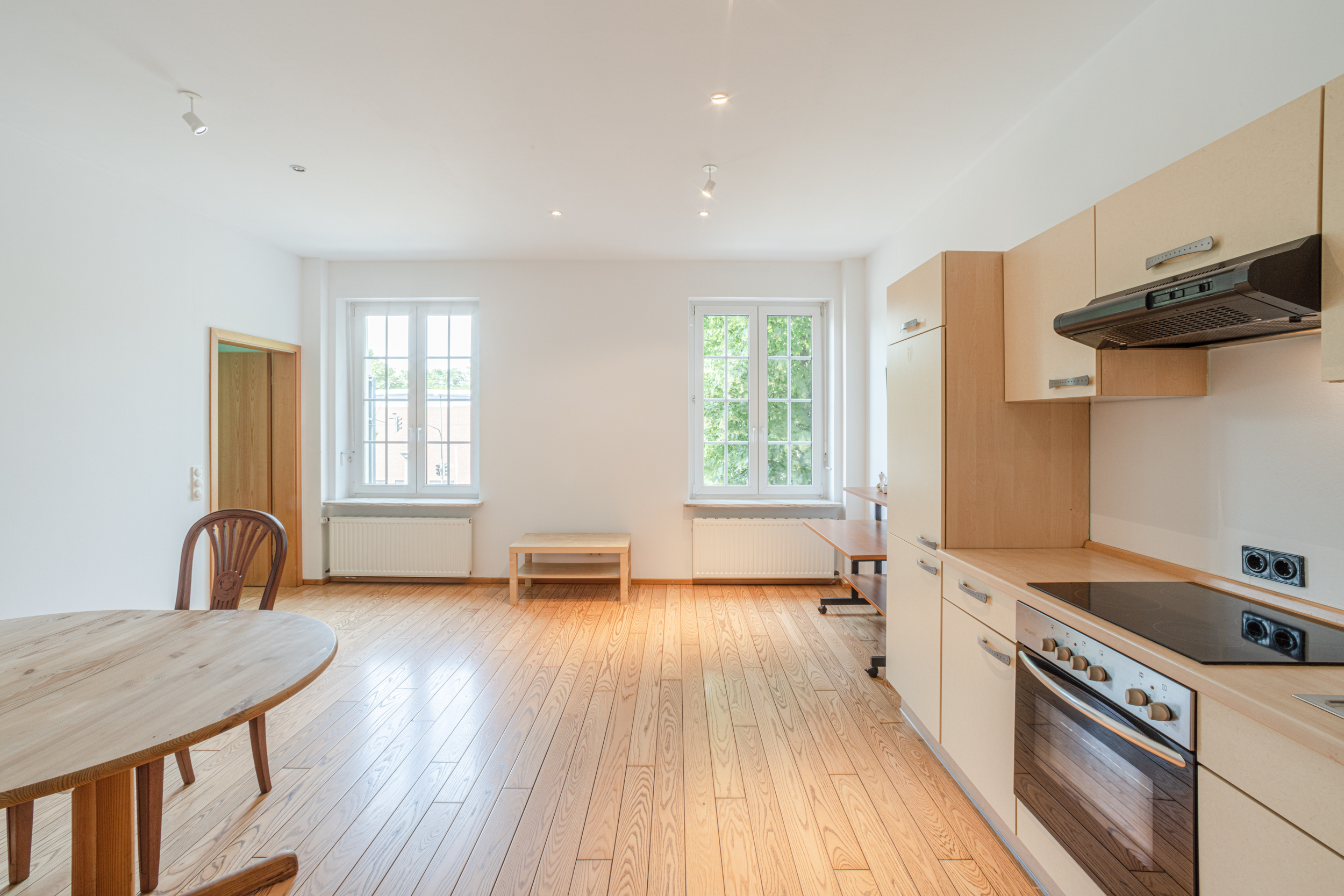 Helles Wohn- und Küchenzimmer mit Holzfußboden, Esstisch, Stühlen und zwei großen Fenstern.