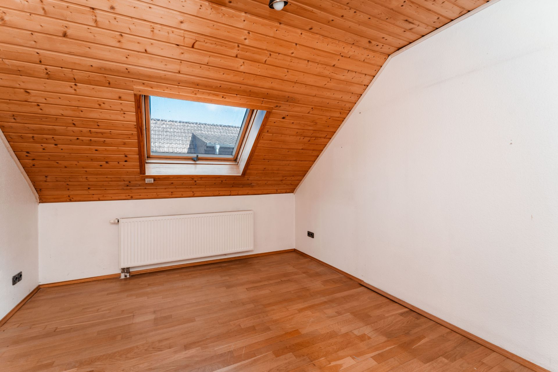 Leerer Raum mit Holzdecke, Dachfenster und Heizkörper unter dem Fenster.