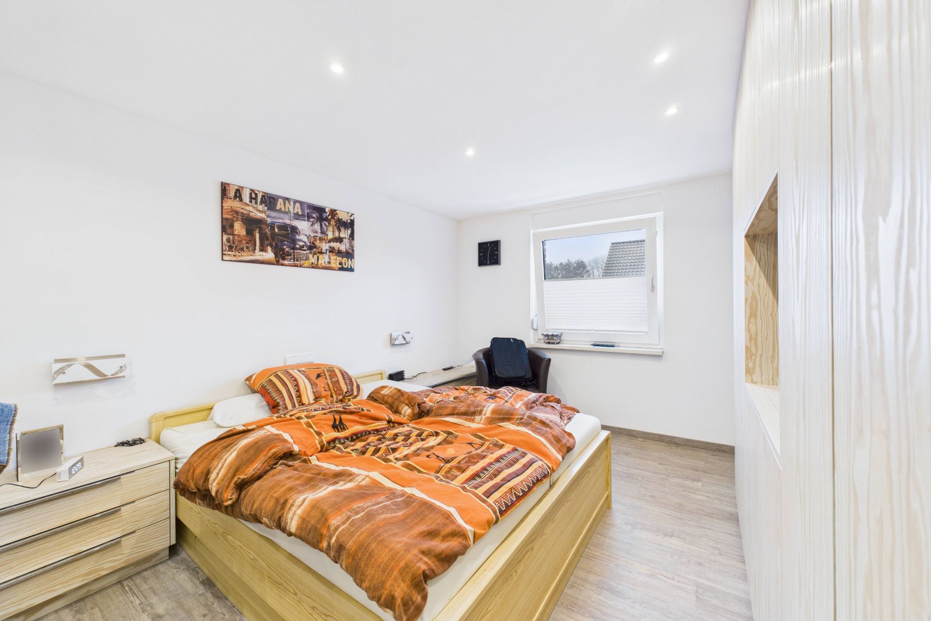 Helles Schlafzimmer mit Doppelbett, Schreibtisch, großem Fenster und Kleiderschrank.