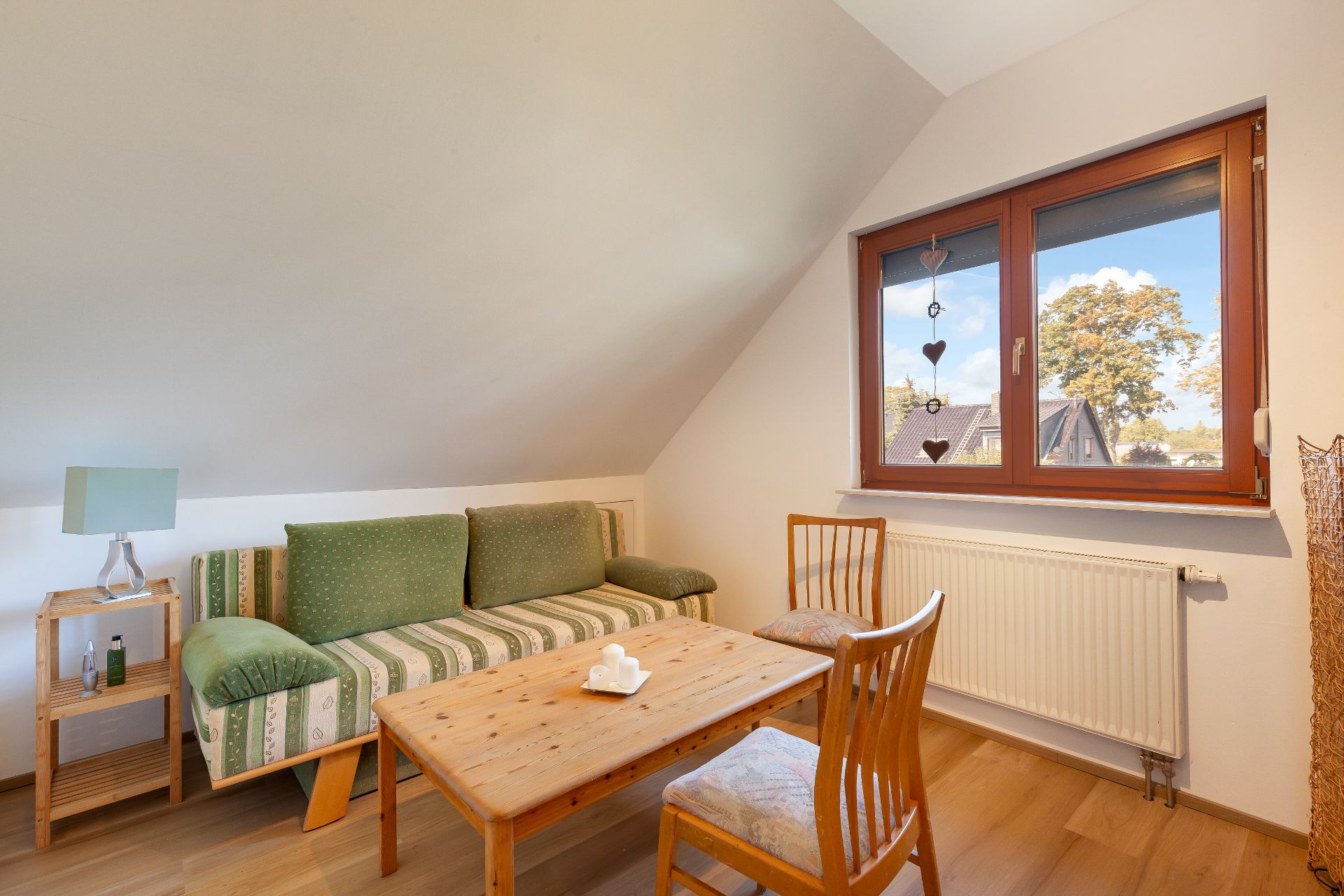 Kleines Wohnzimmer mit grünem Sofa, Holztisch, zwei Stühlen und Fenster.