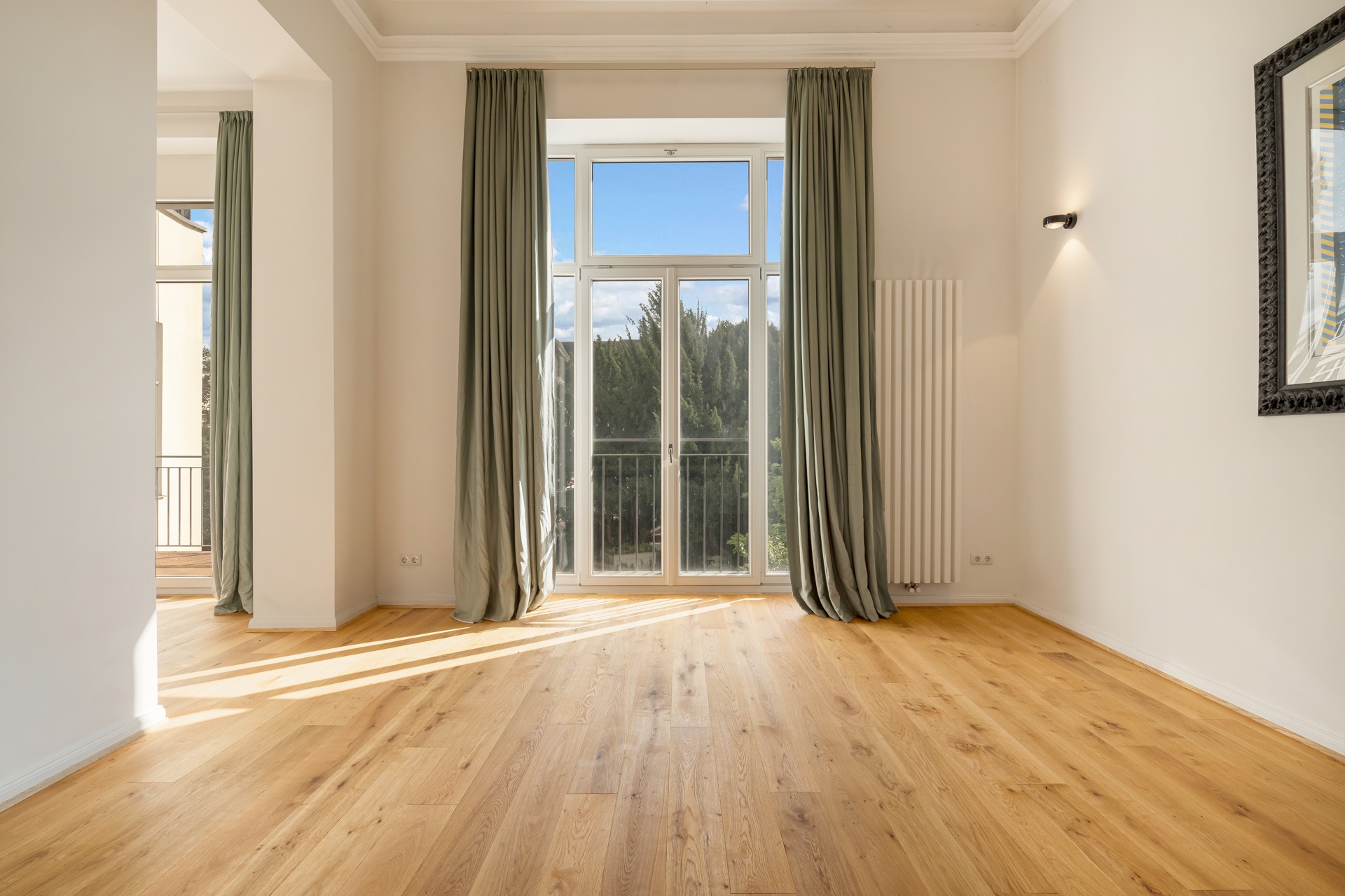 Helles Zimmer mit großen Fenstern, grünen Vorhängen und Holzfußboden.