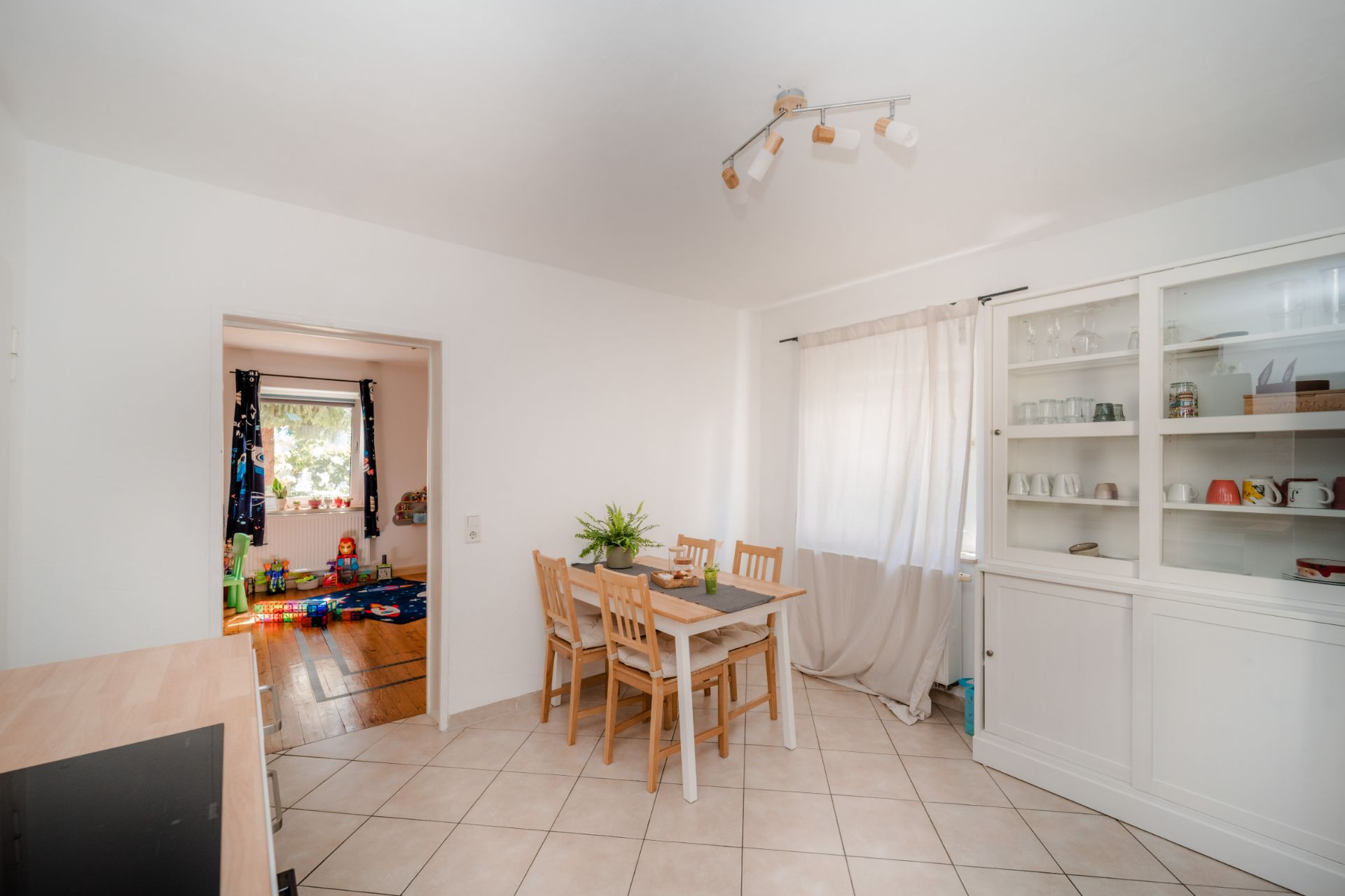 Essbereich mit Holztisch und vier Stühlen, Regal mit Geschirr, Fenster mit Vorhang.