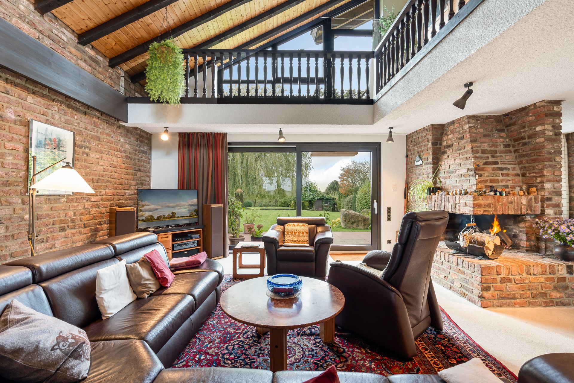 Wohnzimmer mit Ledersofa, gemauertem Kamin, großem Fenster und Blick in den Garten.