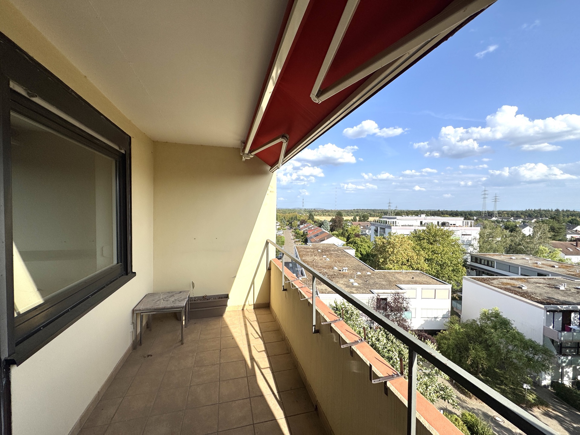 Balkon mit Markise, kleinem Tisch und Blick auf Wohnhäuser und Bäume.